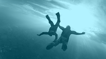 Two skydivers holding each other's leg as they free fall.