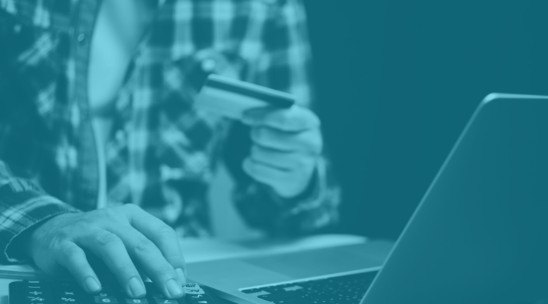 Man sits at laptop and looks at credit card to make online purchase
